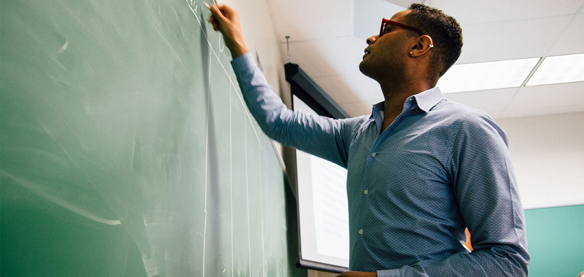 Ezekiel Dixon-Roman teaching a course, writing on a chalkboard.