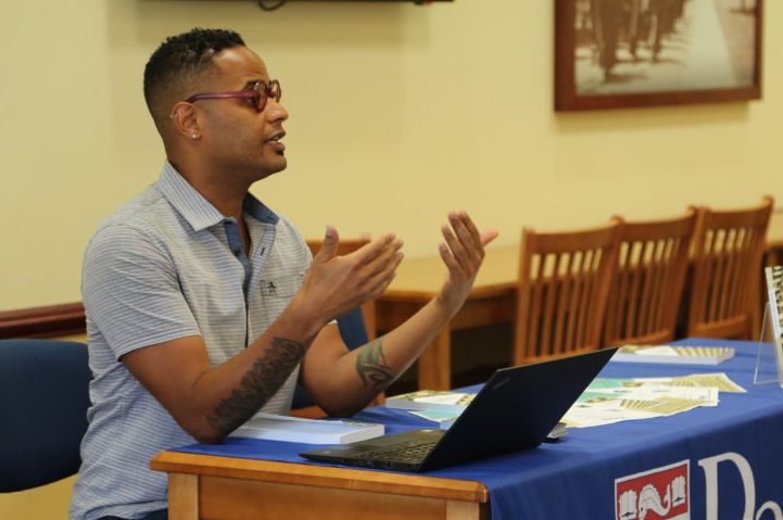 Ezekiel Dixon-Roman sits at a table with a laptop and speaks to an audience