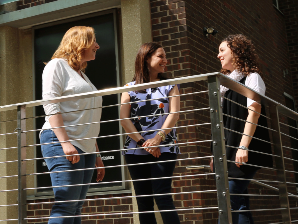 Three women standing outside by a porch railing
