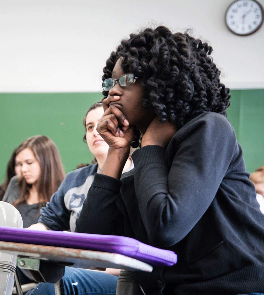 SP2 student with hand resting on chin, listening to lecture in a classroom full of students