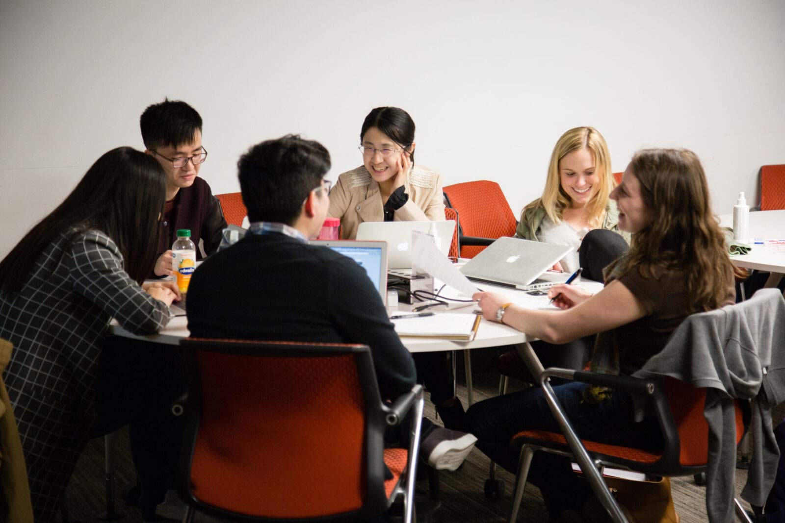 Students sitting around round table smiling with laptops open