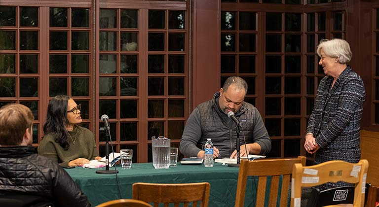 Dean Bachman stands at a table where Ben Jealous signs a book beside Camille Charles