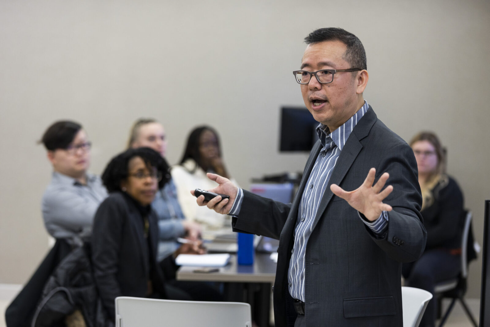 Professor Chao Guo speaks to a class. Several students can be seen listening in the background.