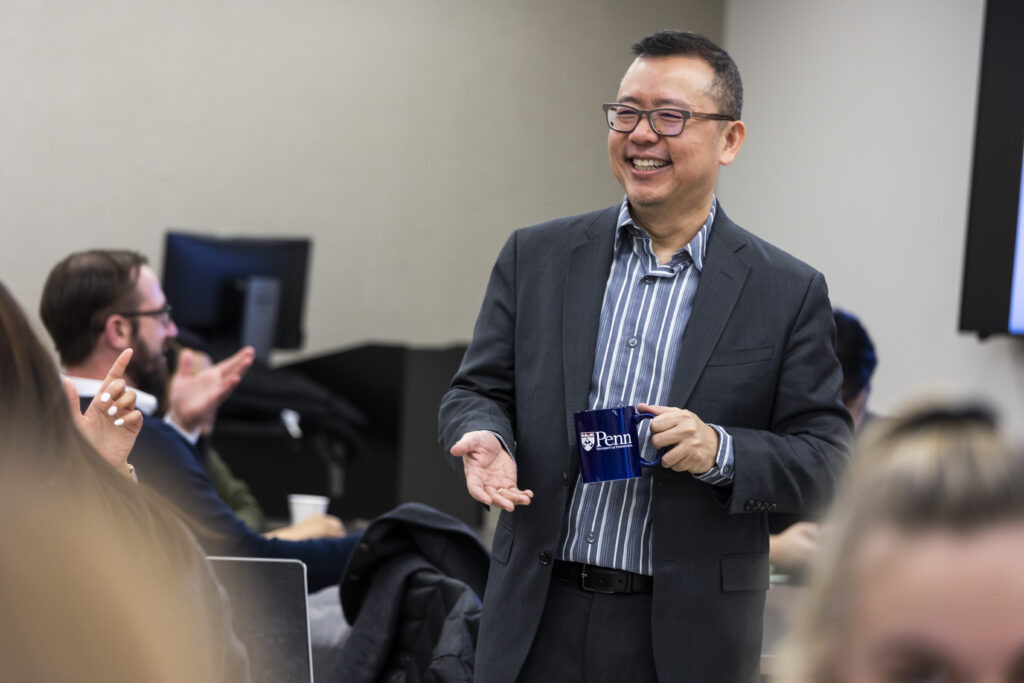 Dr. Chao Guo stands in a classroom holding a Penn mug.