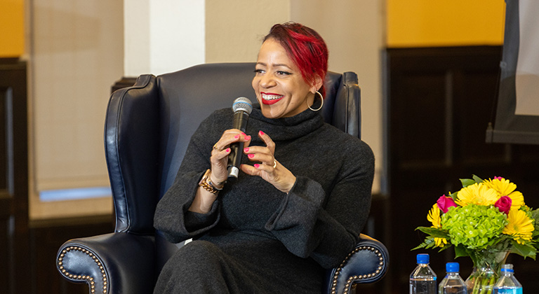 Nikole Hannah-Jones sits onstage holding a microphone and smiling at the audience. 