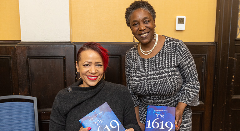 Nikole Hannah-Jones sits at a table and an attendee stands beside her. Both hold copies of The 1619 Project and smile.