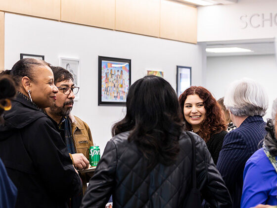 SP2 community members gathered in the center of the lobby with several framed works of art on the wall