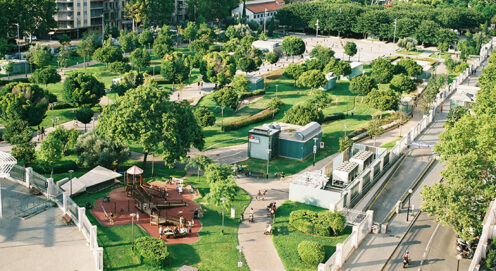 An aerial view of green trees, grass, and a playground bordered by a road and buildings