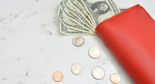 Dollar bills stick out of an orange wallet arranged beside coins on a tabletop