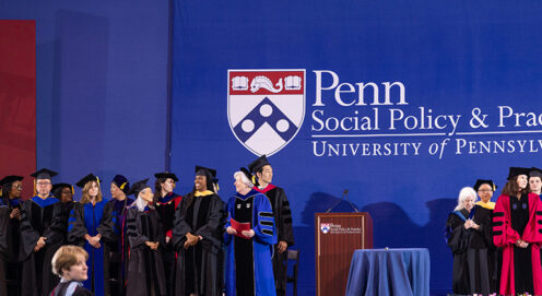 SP2 faculty stand onstage at Commencement in front of a blue background with the School's logo