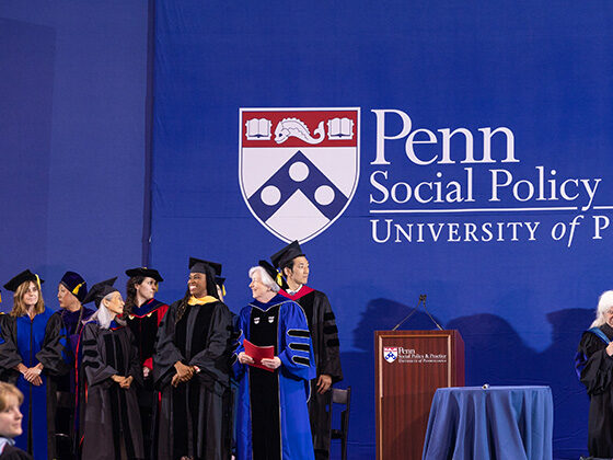 SP2 faculty stand onstage at Commencement in front of a blue background with the School's logo
