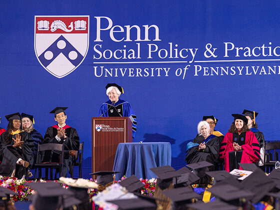 Dean Bachman and SP2's faculty appear onstage at Commencement with the Penn Social Policy & Practice on a blue backdrop behind them