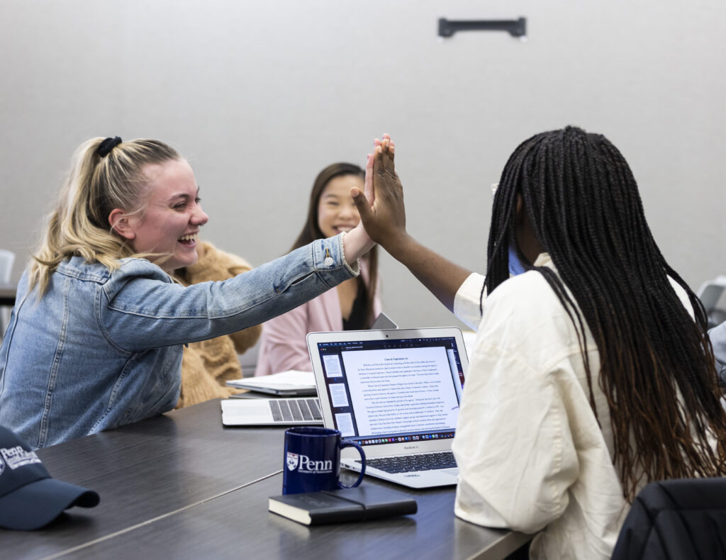 Students high-five over a table with a laptop