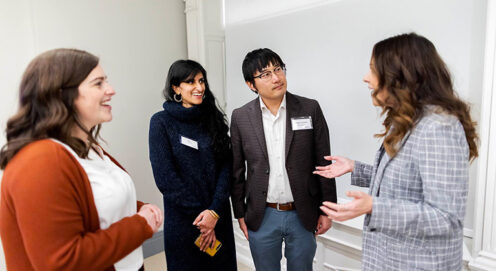 Four graduate students stand together talking near a whiteboard