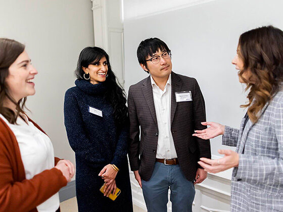 Four graduate students stand together talking near a whiteboard