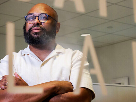 Dr. Patton stands with arms folded behind a window with the word 