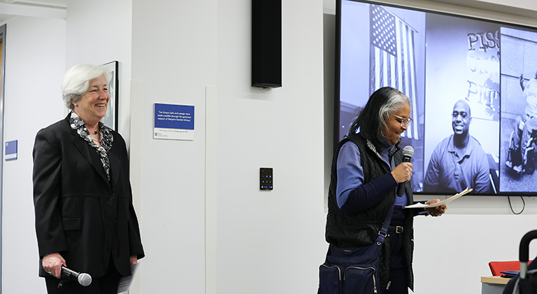 Dean Sally Bachman and Jerri Bourjolly stand beside the Caster lobby screen, where black-and-white photos of the disability rights movement are displayed.