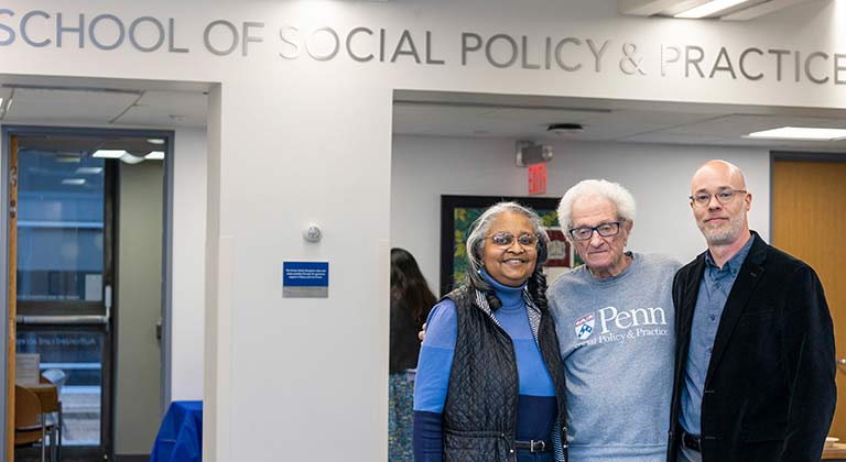 Jerri Bourjolly, Harvey Finkle, and Bart Miltenberger stand together smiling below the lobby sign "SCHOOL OF SOCIAL POLICY & PRACTICE"