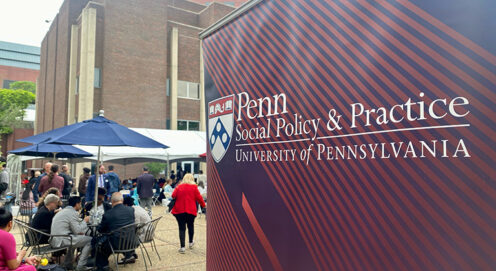 A red banner with the SP2 logo appears outdoors in the foreground, with a gathering in the courtyard in the background