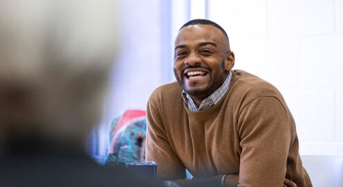 DeMarcus Jenkins sits at a table in a classroom, leaning forward and smiling