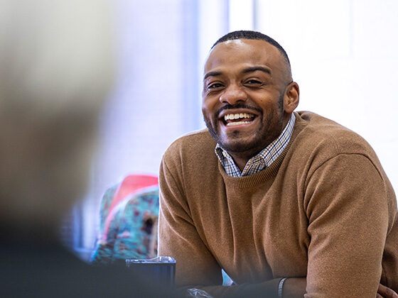 DeMarcus Jenkins sits at a table in a classroom, leaning forward and smiling