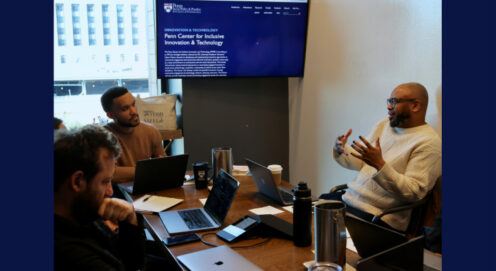 Desmond Patton sits speaking with colleagues at a table. In the background, a screen reads 