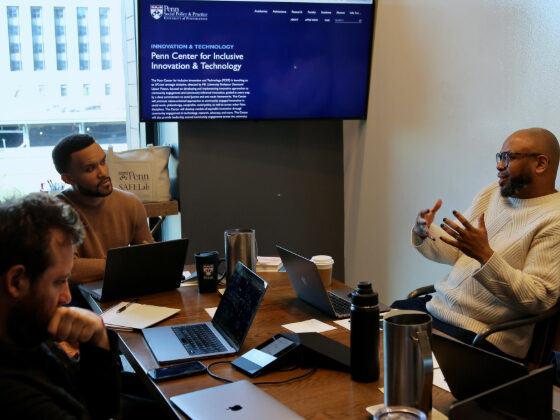 Desmond Patton sits speaking with colleagues at a table. In the background, a screen reads 