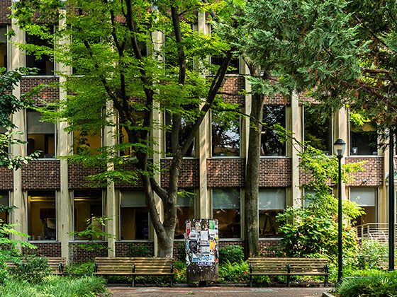 SP2's Caster building is pictured from the opposite side of Locust Walk, with green trees and plants around and against the building.