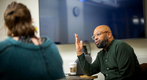 At a classroom table, Desmond Patton speaks to a student