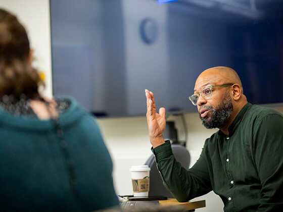 At a classroom table, Desmond Patton speaks to a student