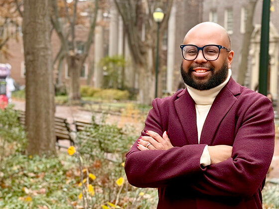 Desmond Patton stands beside Locust Walk, arms folded