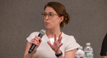 Sharon Zanti sits at a table speaking into a microphone