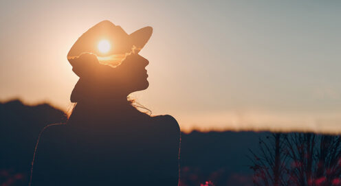 Photo of a woman silhouetted against a sunset, with the sun visible through her profile