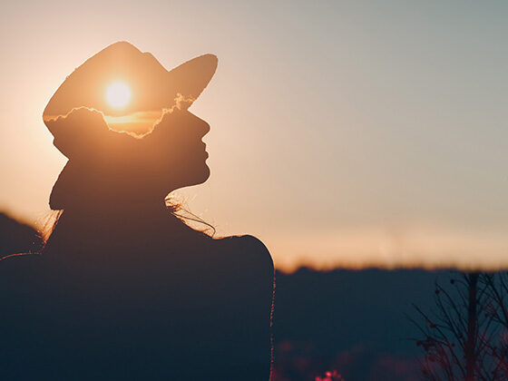 Photo of a woman silhouetted against a sunset, with the sun visible through her profile