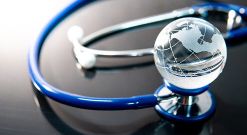 On a glossy surface, a small glass globe sits on a blue stethoscope