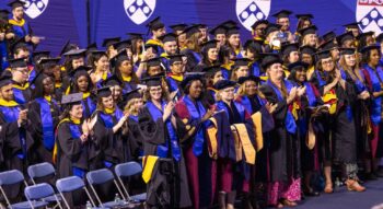 SP2 graduates standing and clapping in the Palestra.
