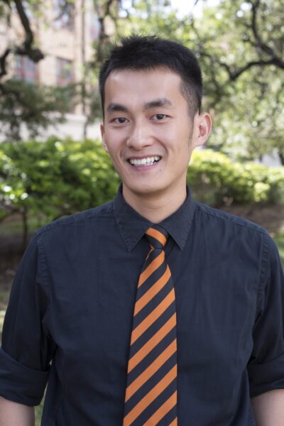 Portrait of Anao Zhang in a black shirt and striped tie foregrounded against the backdrop of nature