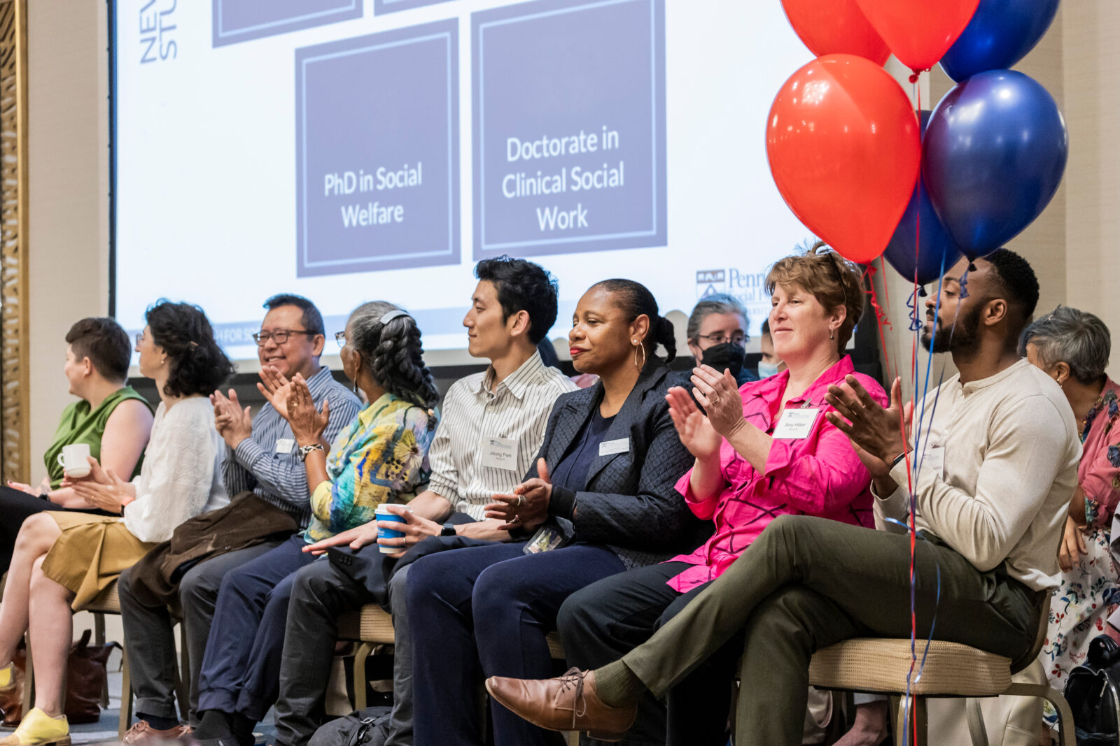 A photo of faculty seated in front a powerpoint presentation at SP2 2024 Convocation, red balloons in the foreground