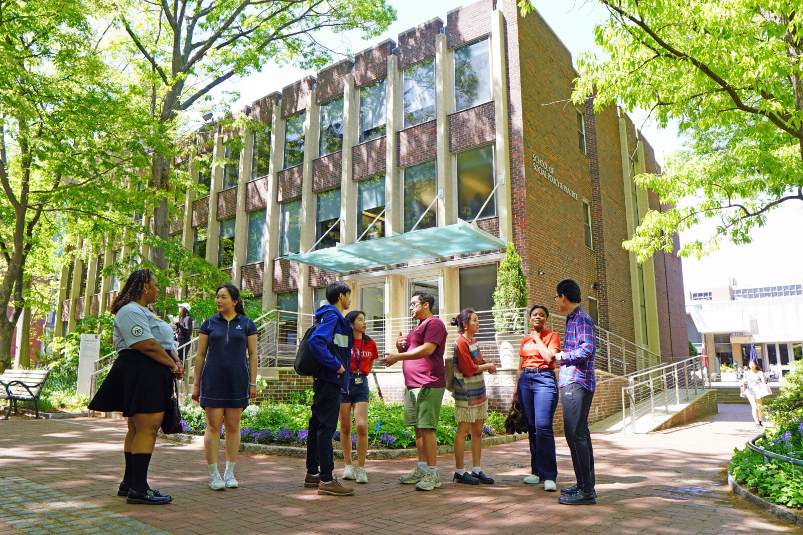 eight students of varying ages, genders, and demographics chat in front of the Caster Building
